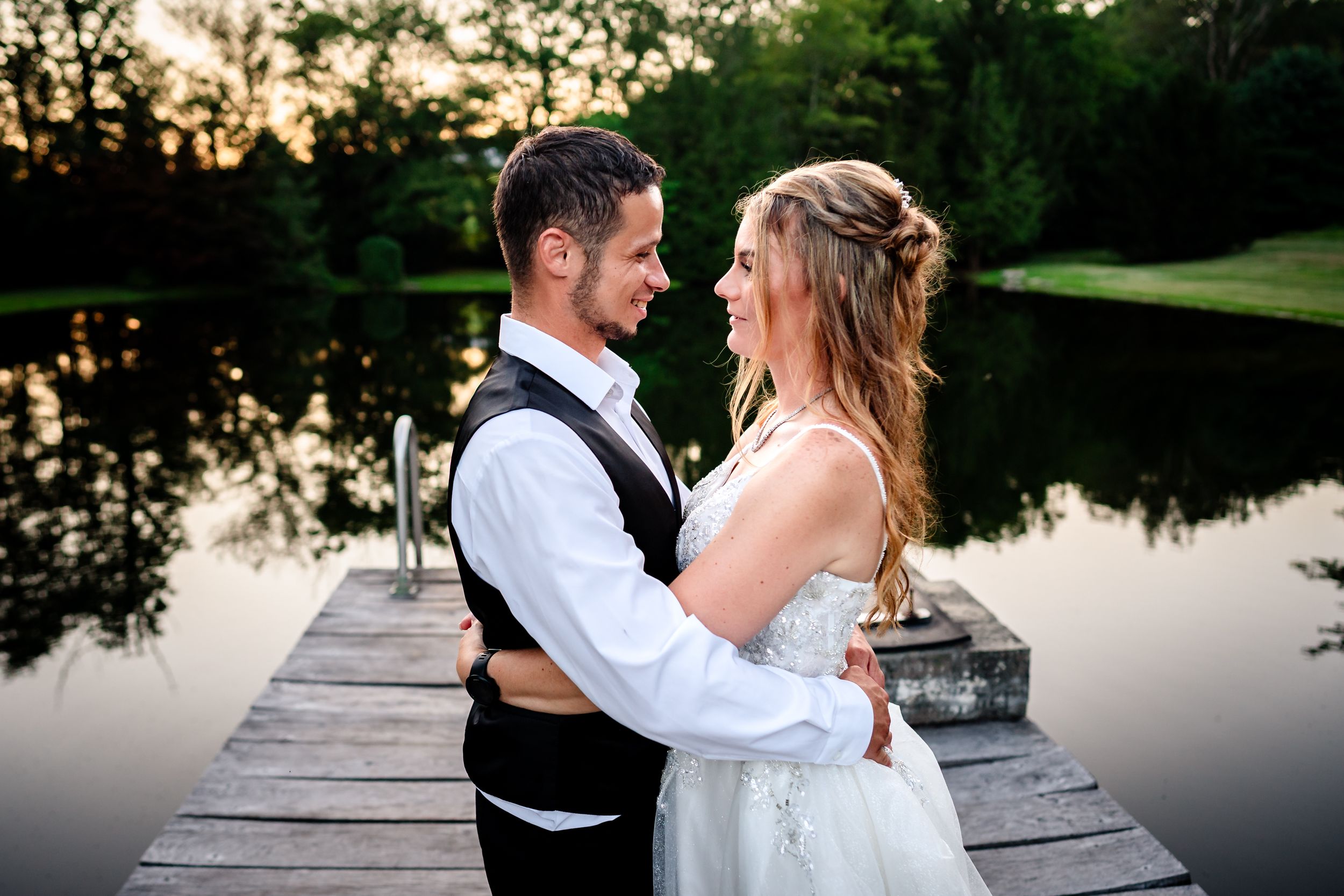 A romantic couple embraces on a wooden dock at dusk with a serene lake in the background.