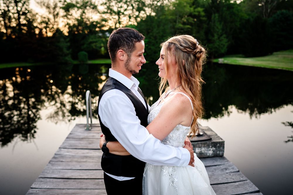 A romantic couple embraces on a wooden dock at dusk with a serene lake in the background.