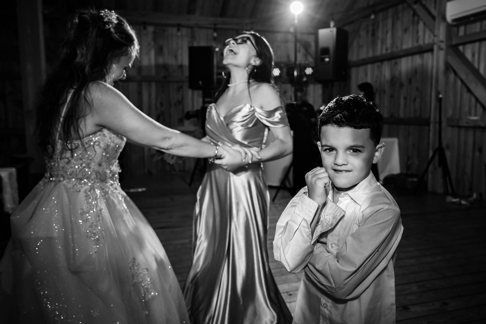 Wedding party dances together in a rustic barn venue with string lights creating a warm atmosphere.
