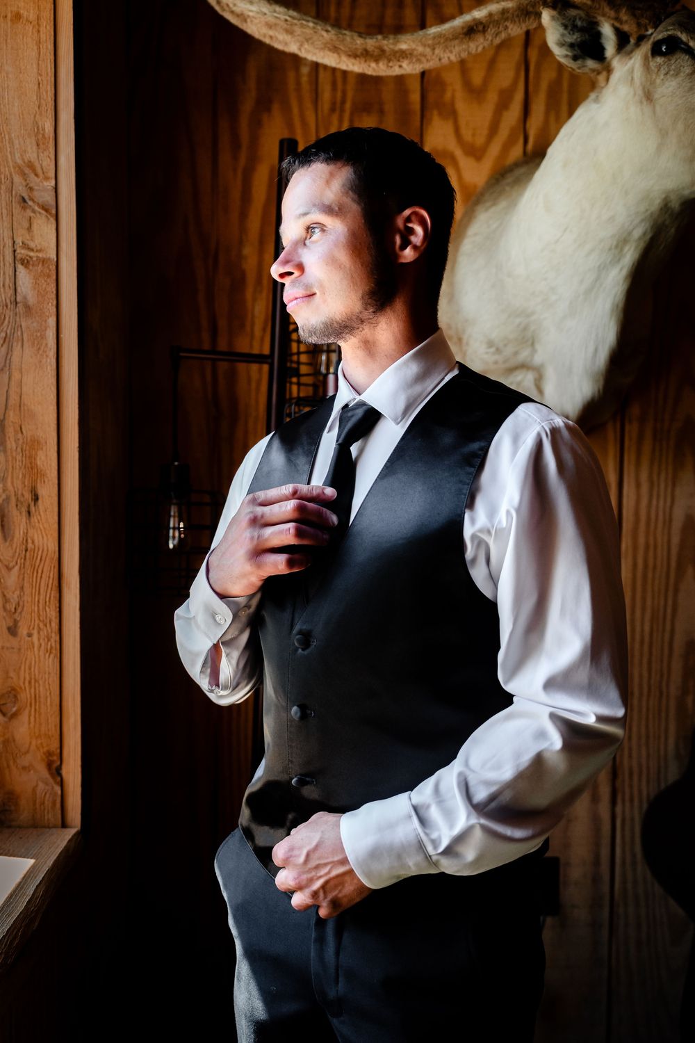 Person in formal attire standing in rustic wooden room with dramatic lighting.
