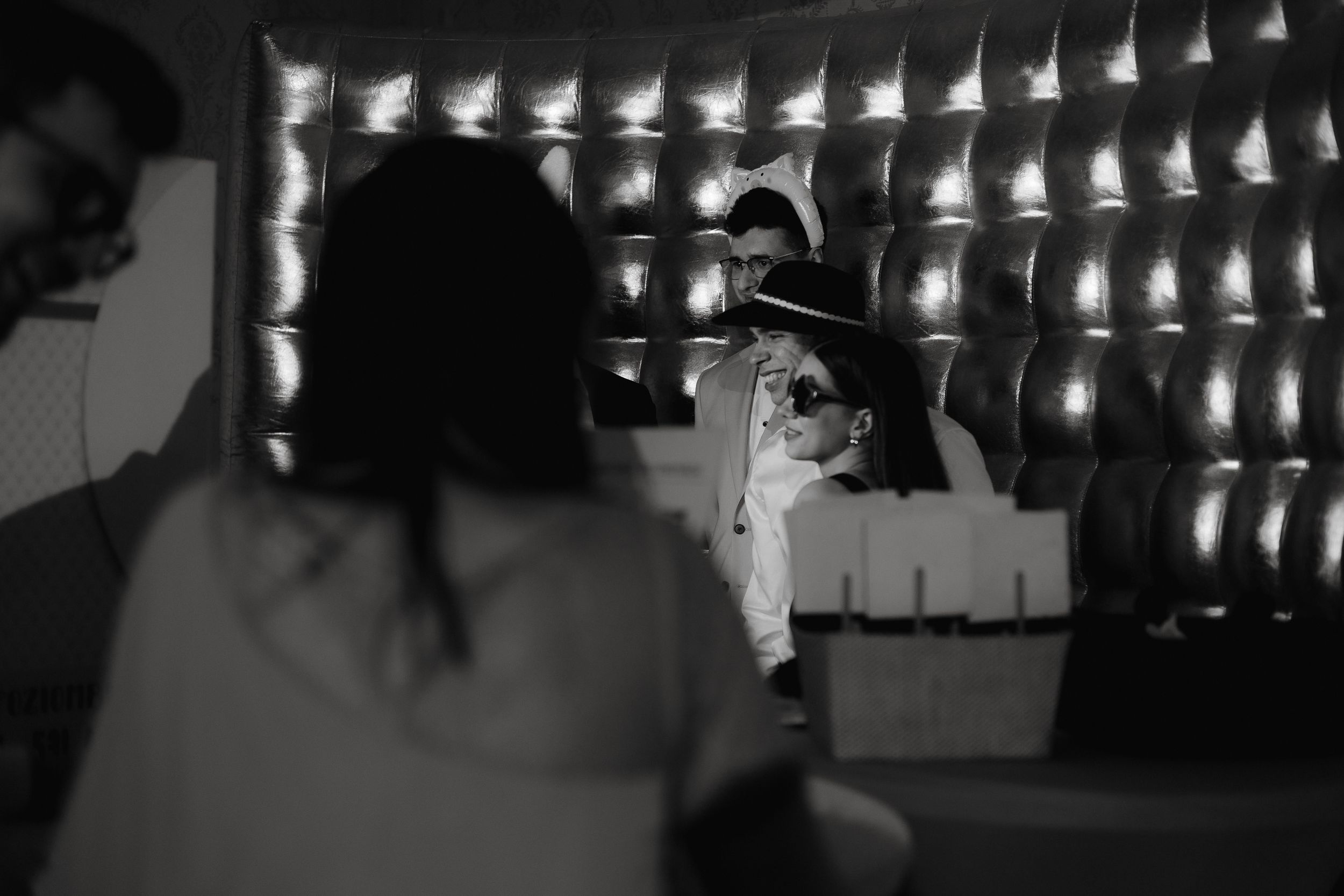 A black and white scene with silhouettes of party guests under a string of lights at an evening celebration.