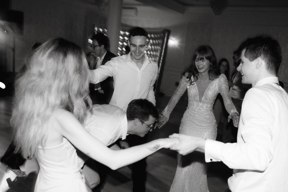 Wedding guests dance together on a dimly lit dance floor during an evening reception celebration.