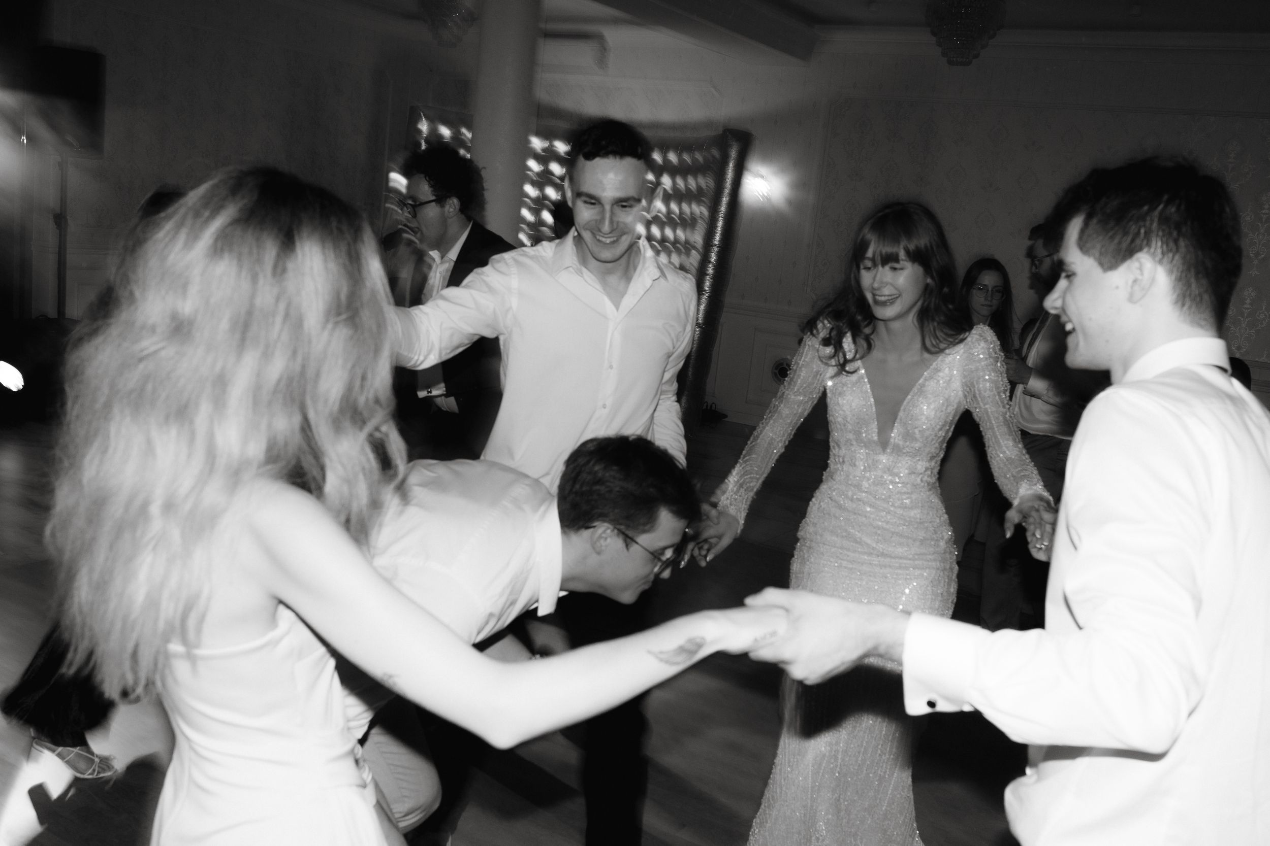 Wedding guests dance together on a dimly lit dance floor during an evening reception celebration.