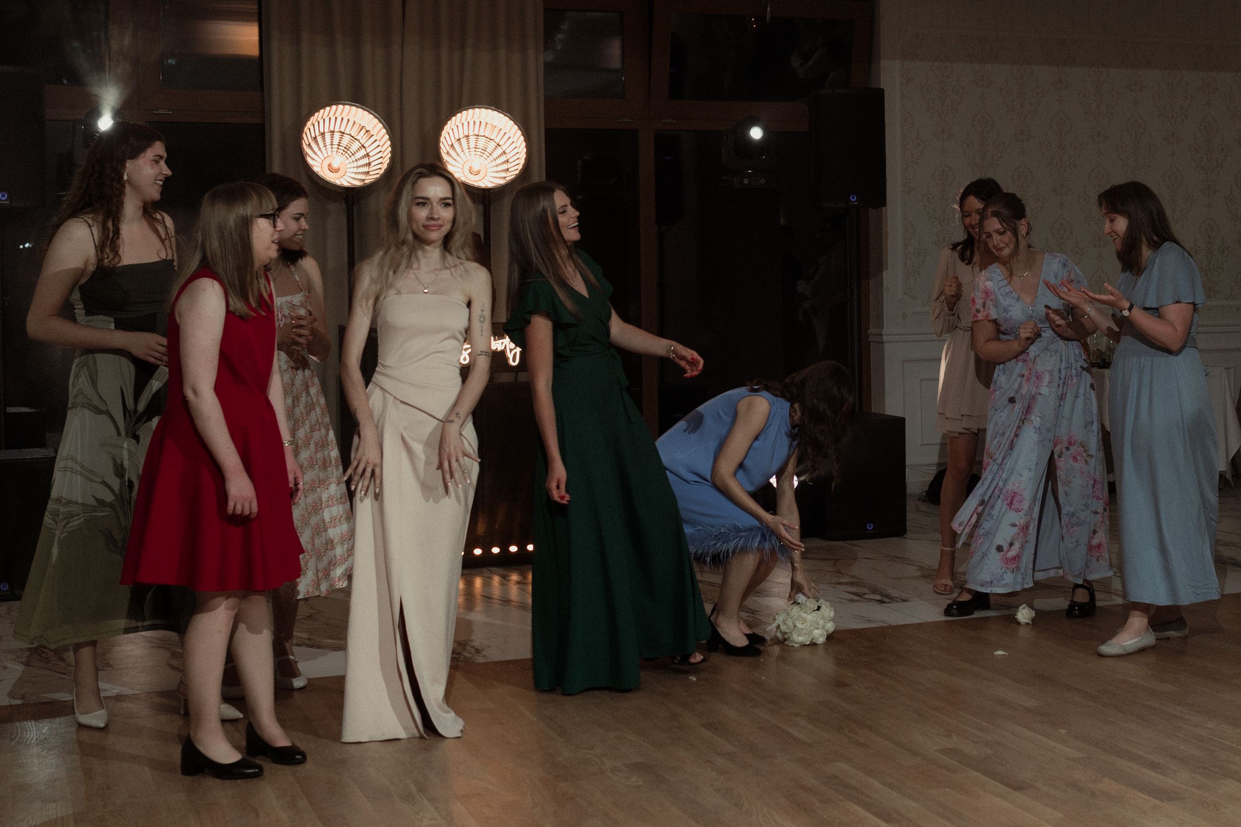 A group of people dressed in formal attire gather on a dimly lit dance floor at an evening celebration.