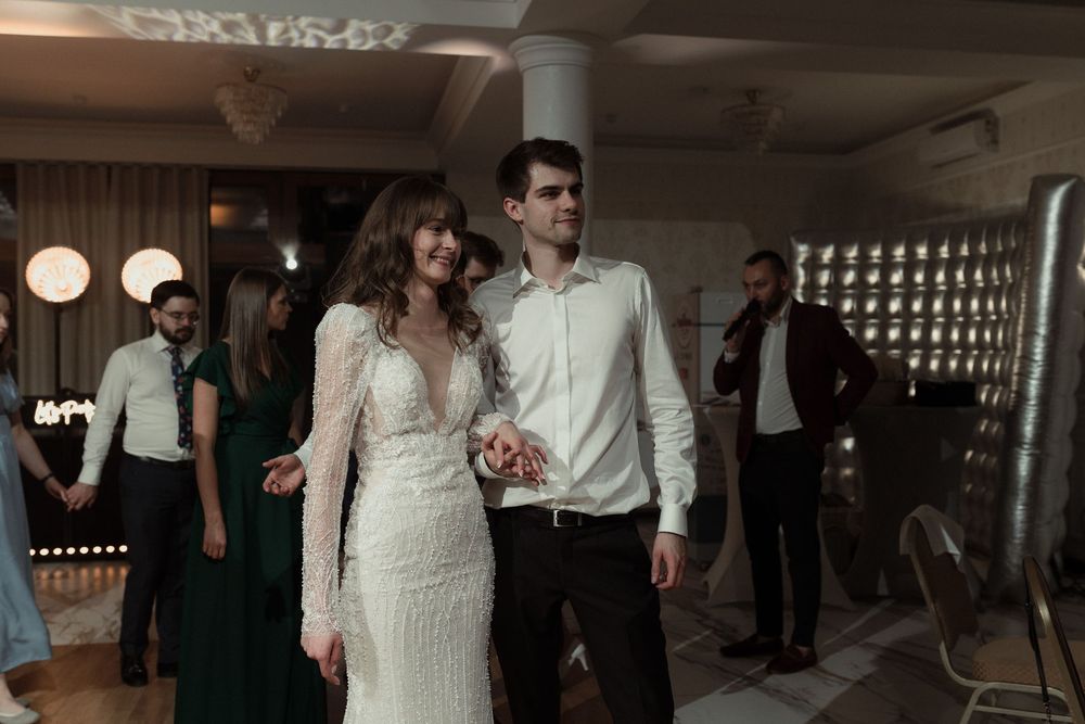 A couple dancing together at an indoor reception venue with decorative lighting and guests in the background.
