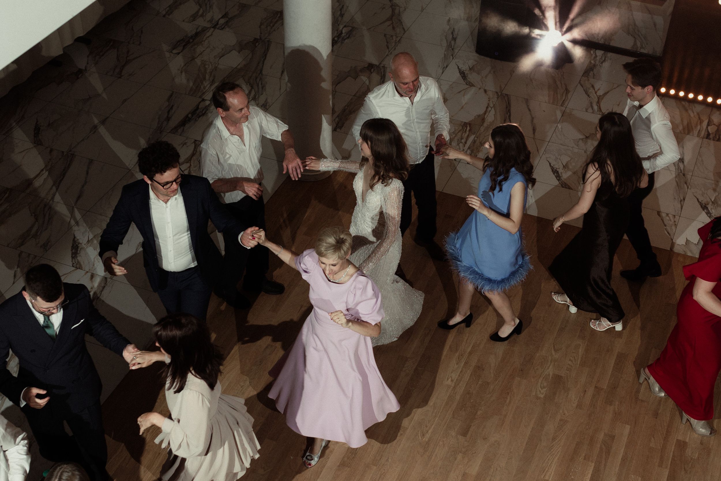 People dancing together during a celebration on a wooden dance floor under ambient lighting.