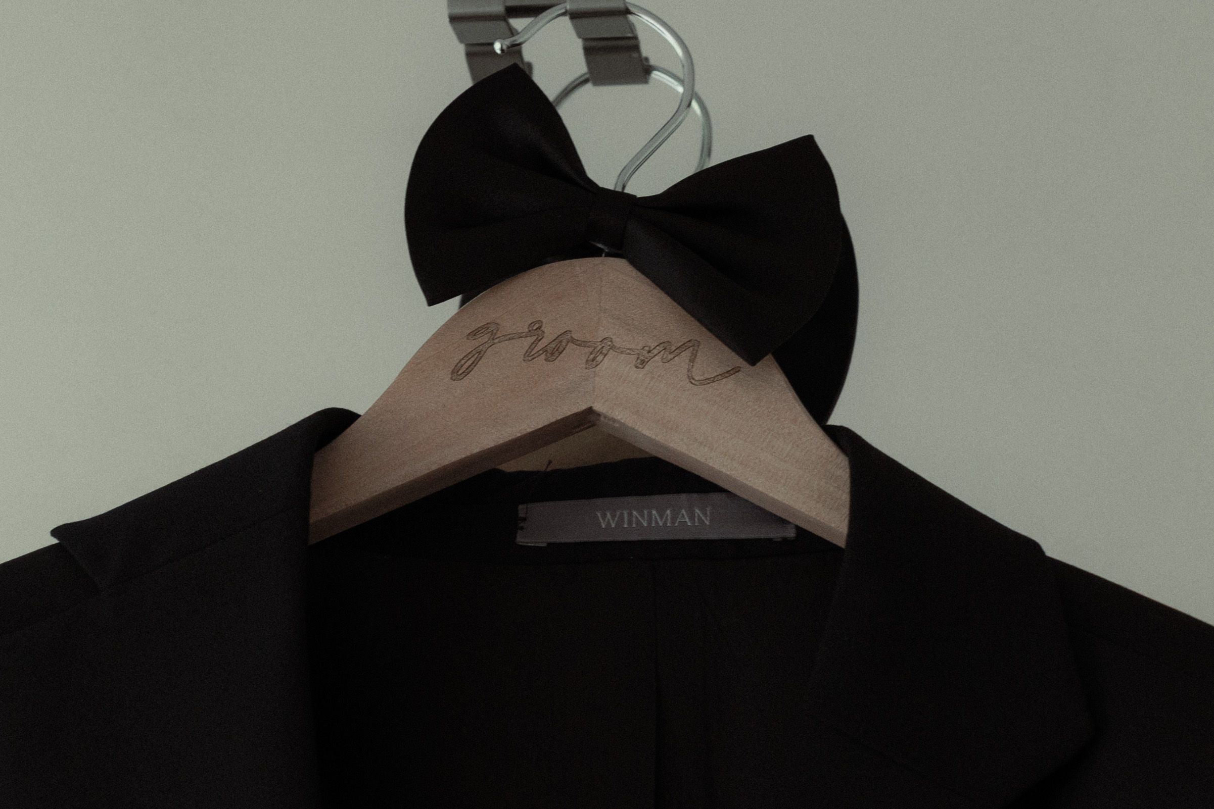 A black bow tie rests on a beige wooden hanger against a dark garment.