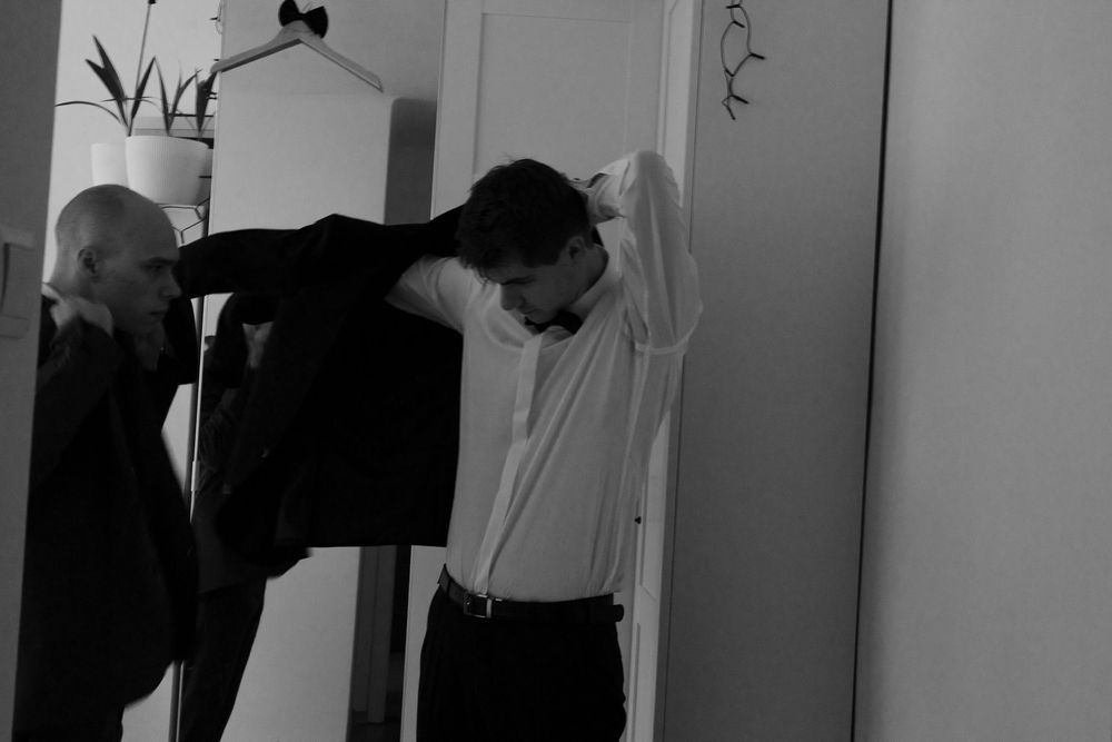 Black and white photo showing someone adjusting formal attire in front of a wardrobe.