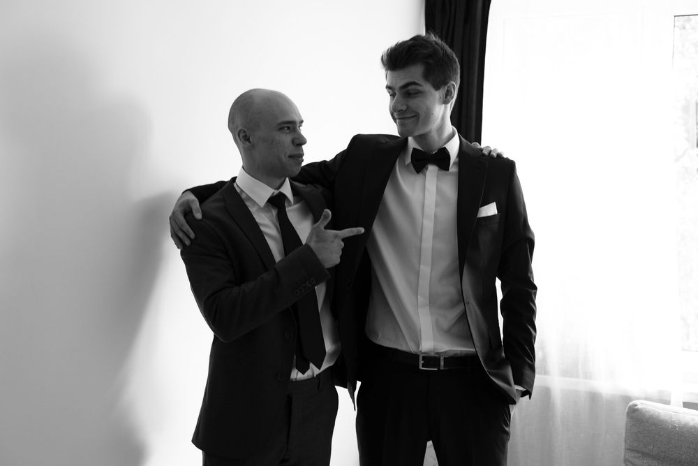 Two people wearing formal suits and bow ties having a conversation in black and white.