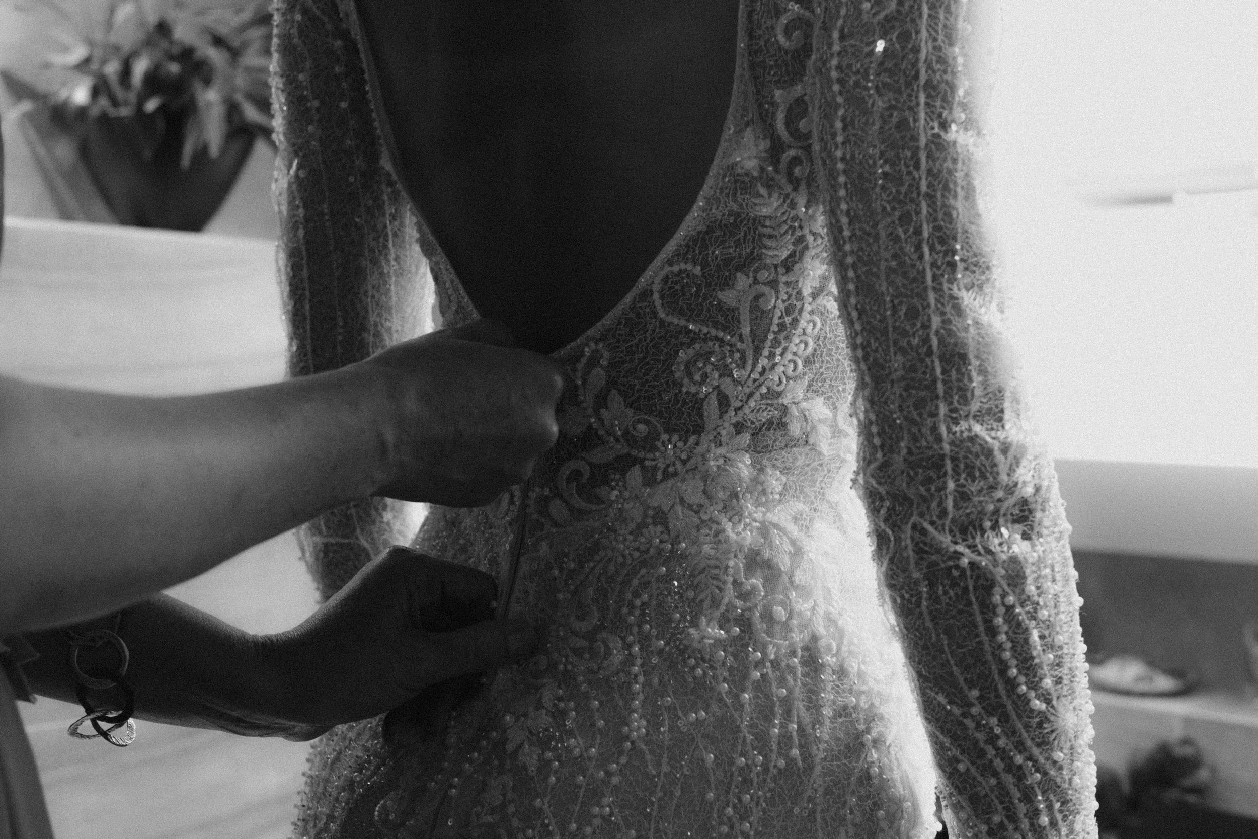 Close-up black and white image of hands adjusting a delicate lace wedding dress during final fitting preparations.
