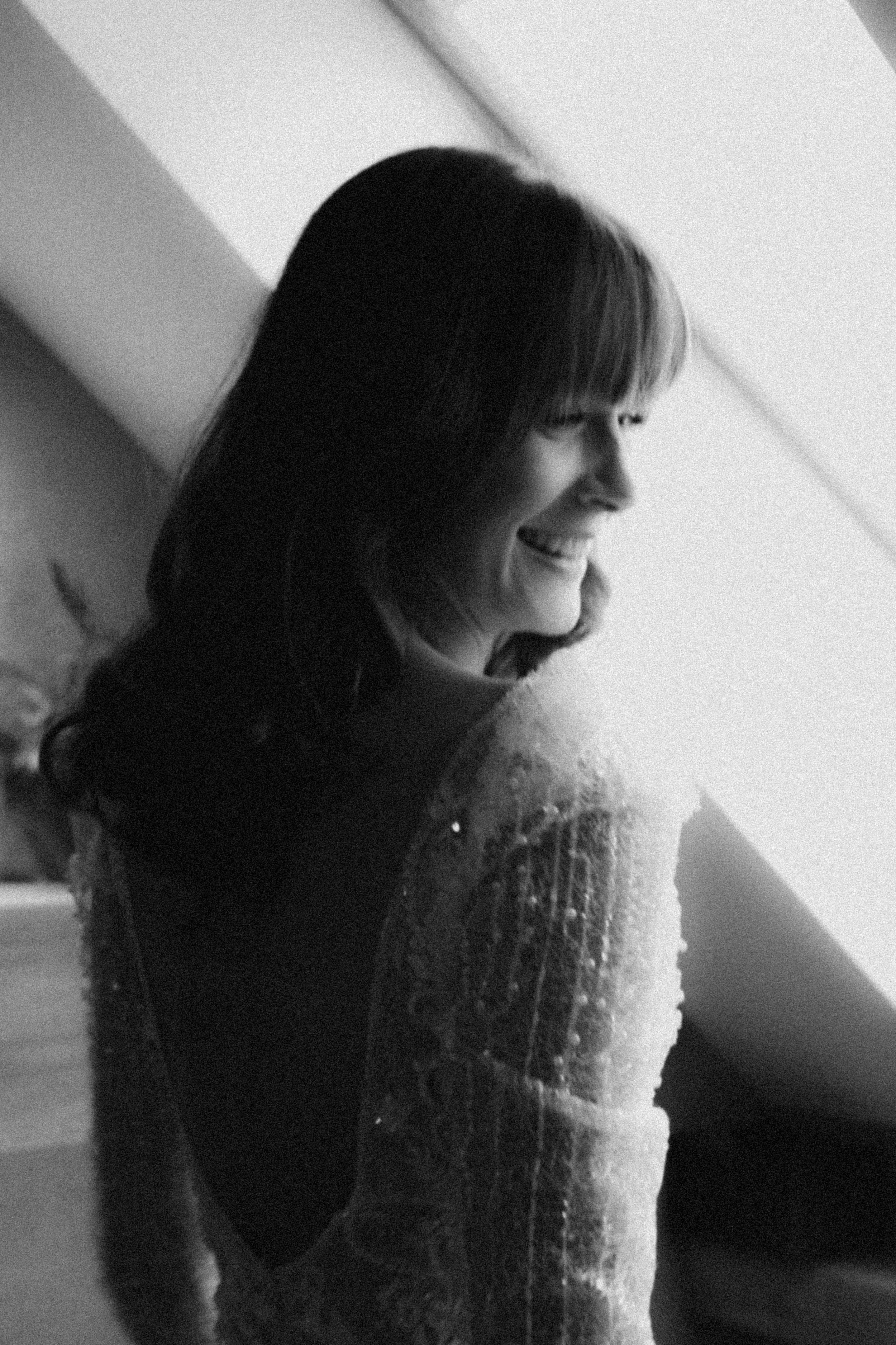 A candid black and white profile shot of someone in a lacy sleeve dress laughing while looking to the side.