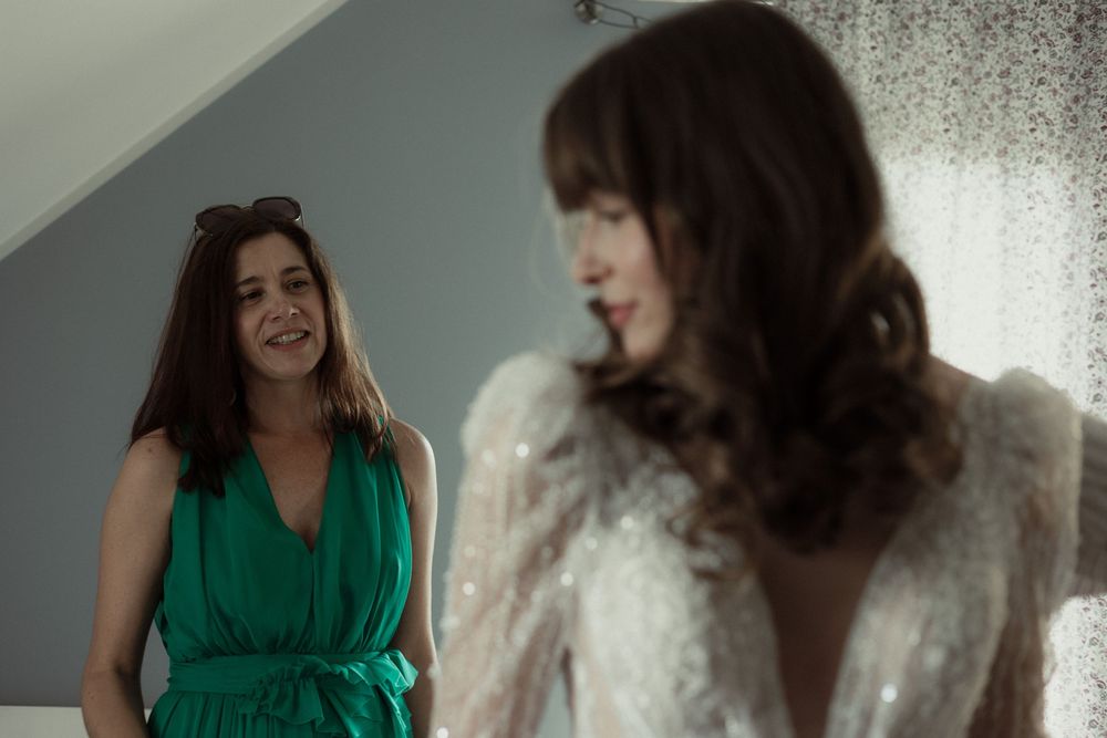 Two people in formal attire laugh together during a photo session in front of a light colored wall.