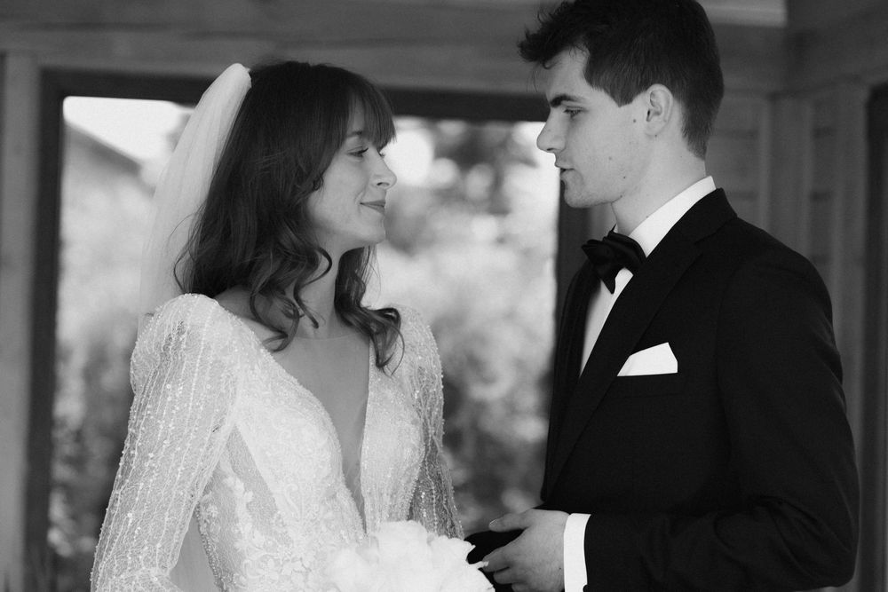 A bride and groom stand inches apart beneath a floral arch at their outdoor wedding ceremony.