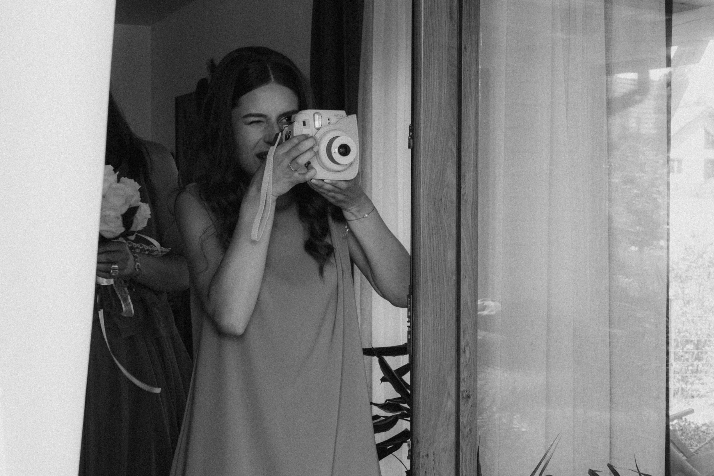 A black and white photo shows someone taking pictures in a mirror with a film camera and flash.