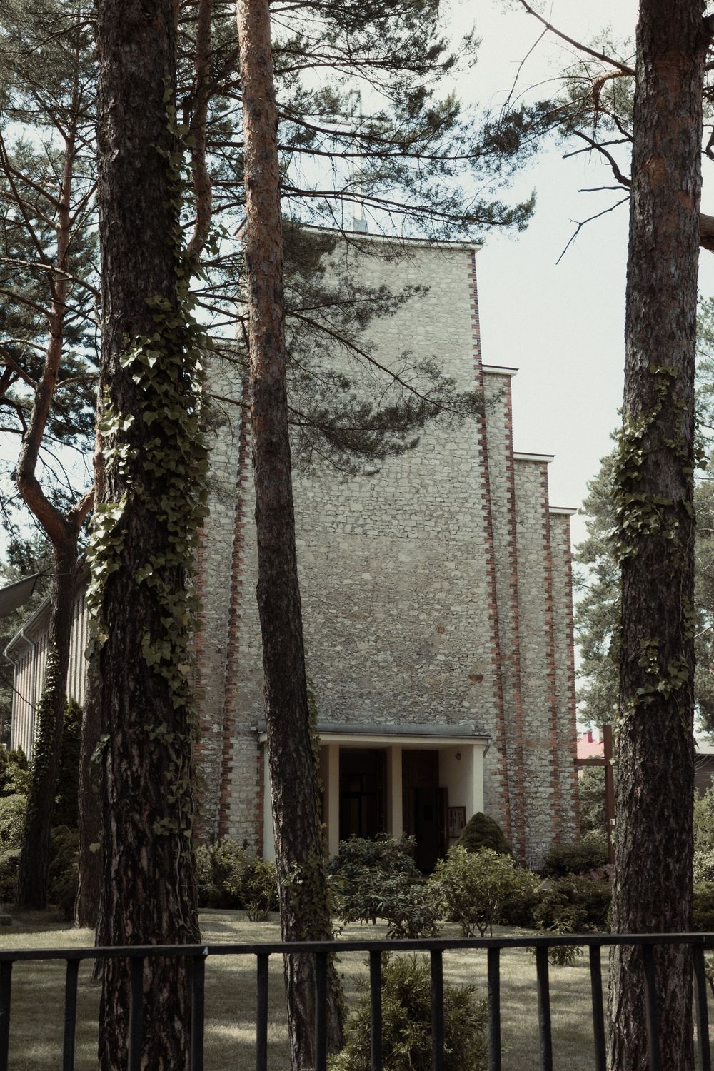 Modern stepped brick church facade framed by tall pine trees against an overcast sky.