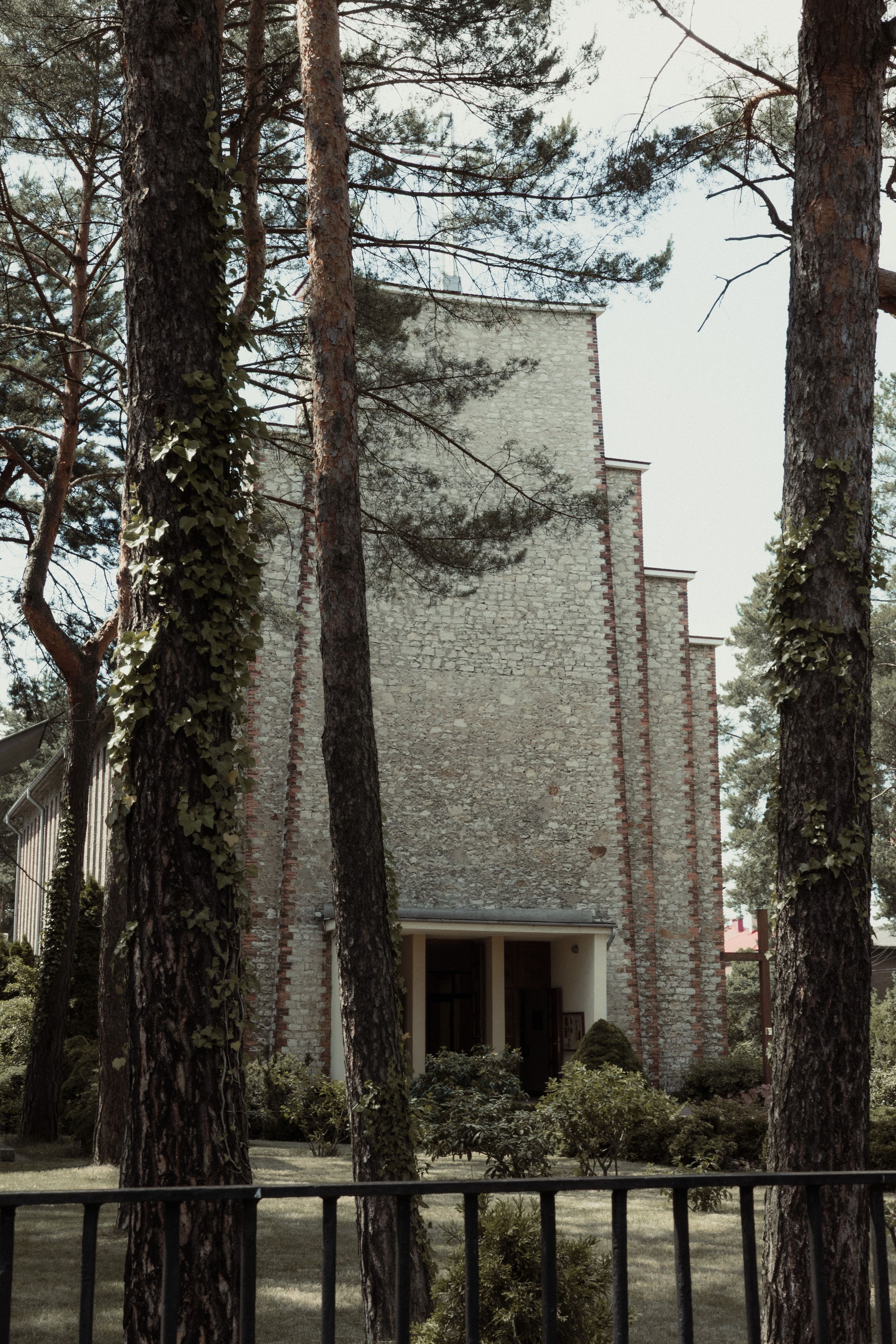 Modern stepped brick church facade framed by tall pine trees against an overcast sky.