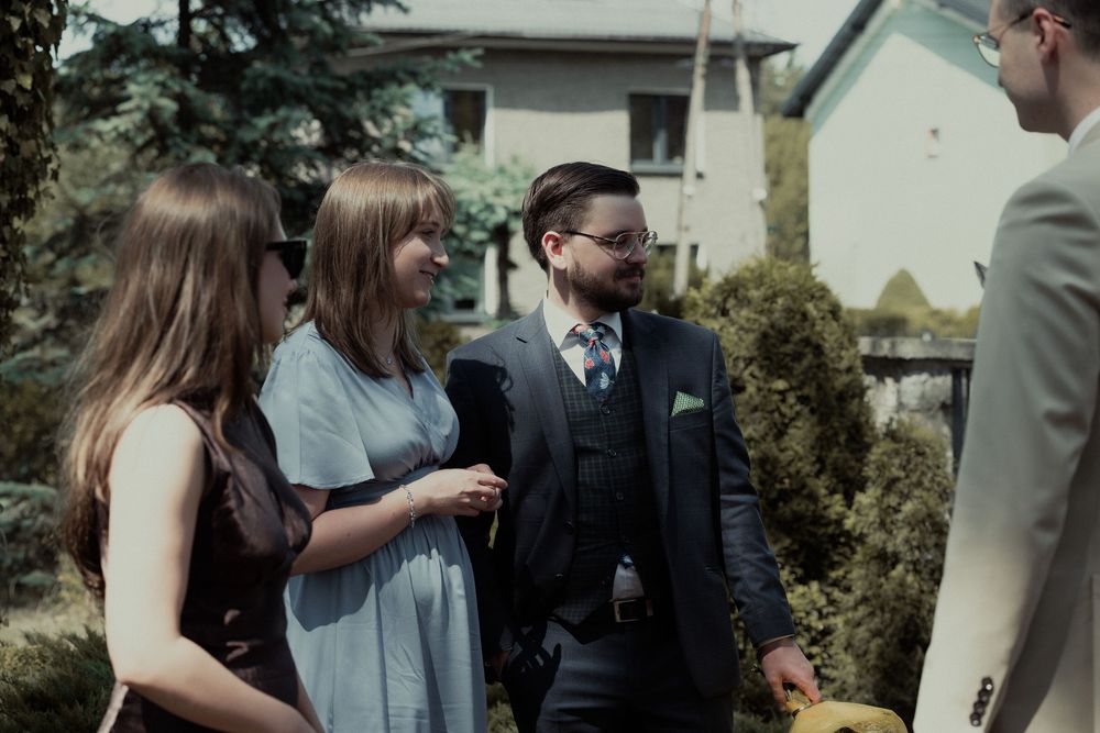 People are greeting each other at an outdoor gathering wearing formal attire in a backyard setting.