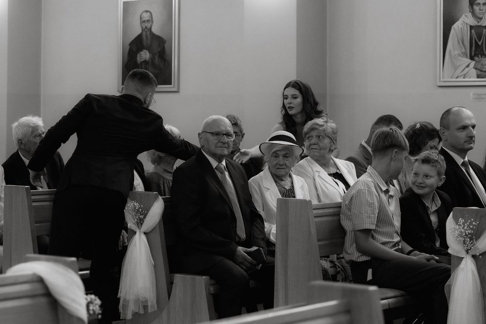 People seated in church pews during a service with portraits hanging on the wall in black and white photograph.