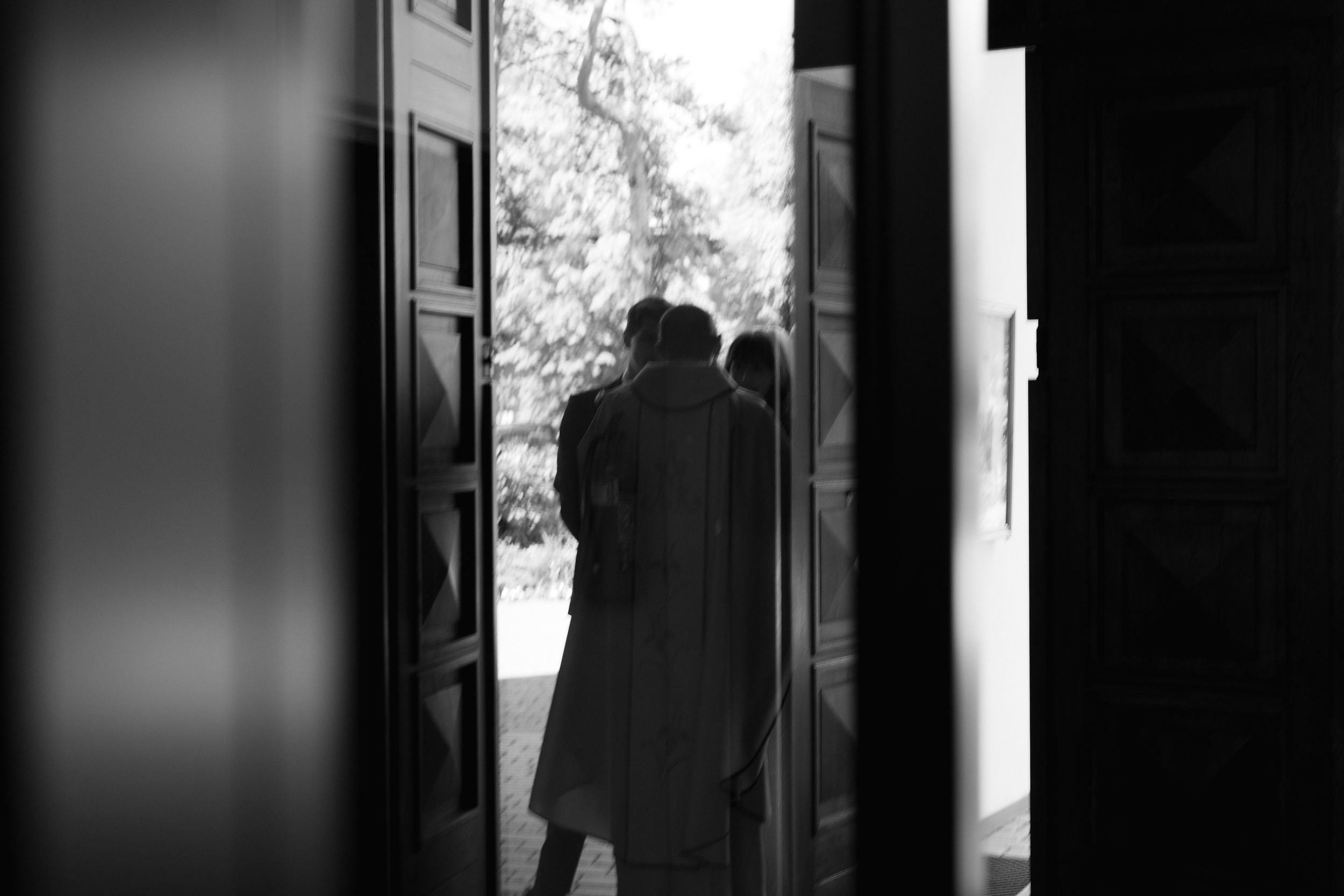 A dark silhouette stands in a doorway creating contrast between light and shadow through vertical architectural framing.