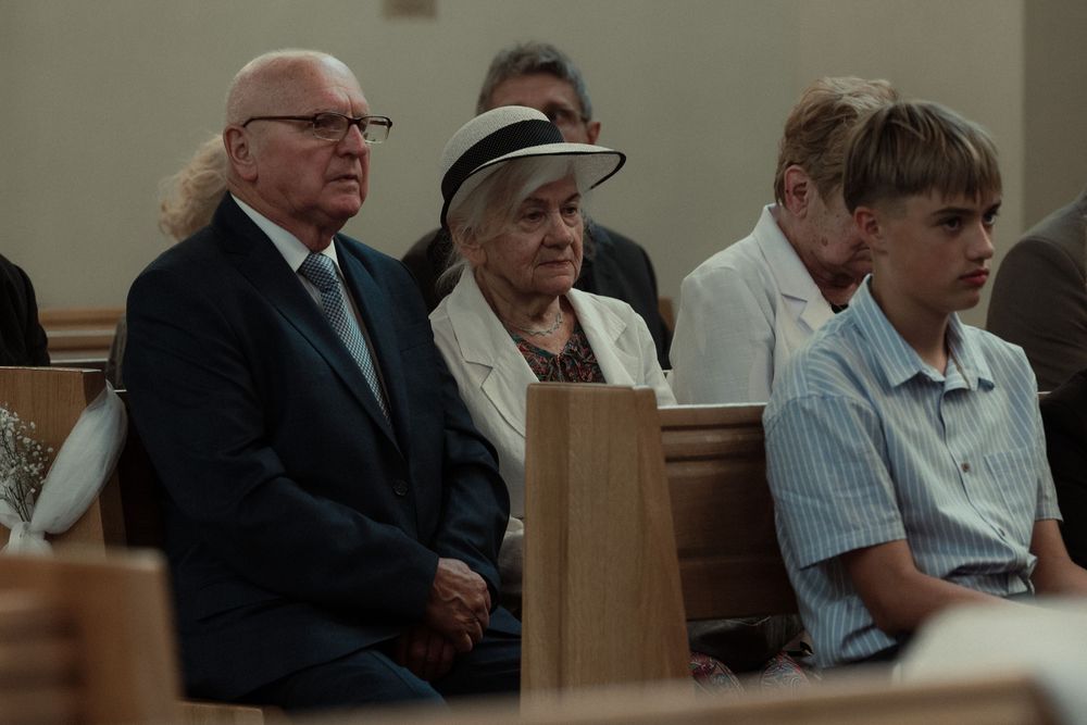Three people sit together in a church pew during a service, wearing casual attire.