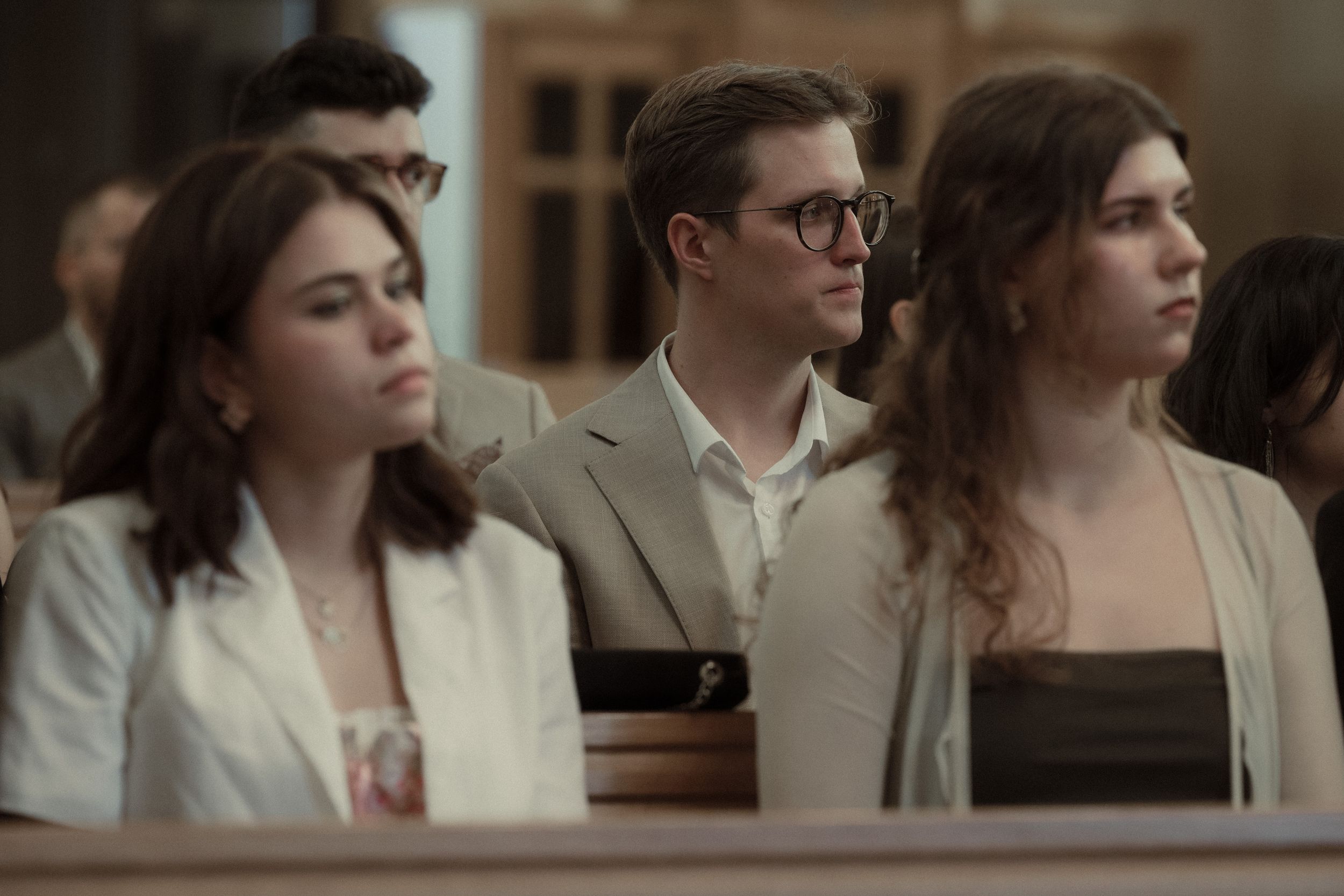 People sit together in a church pew during a ceremony wearing formal attire.