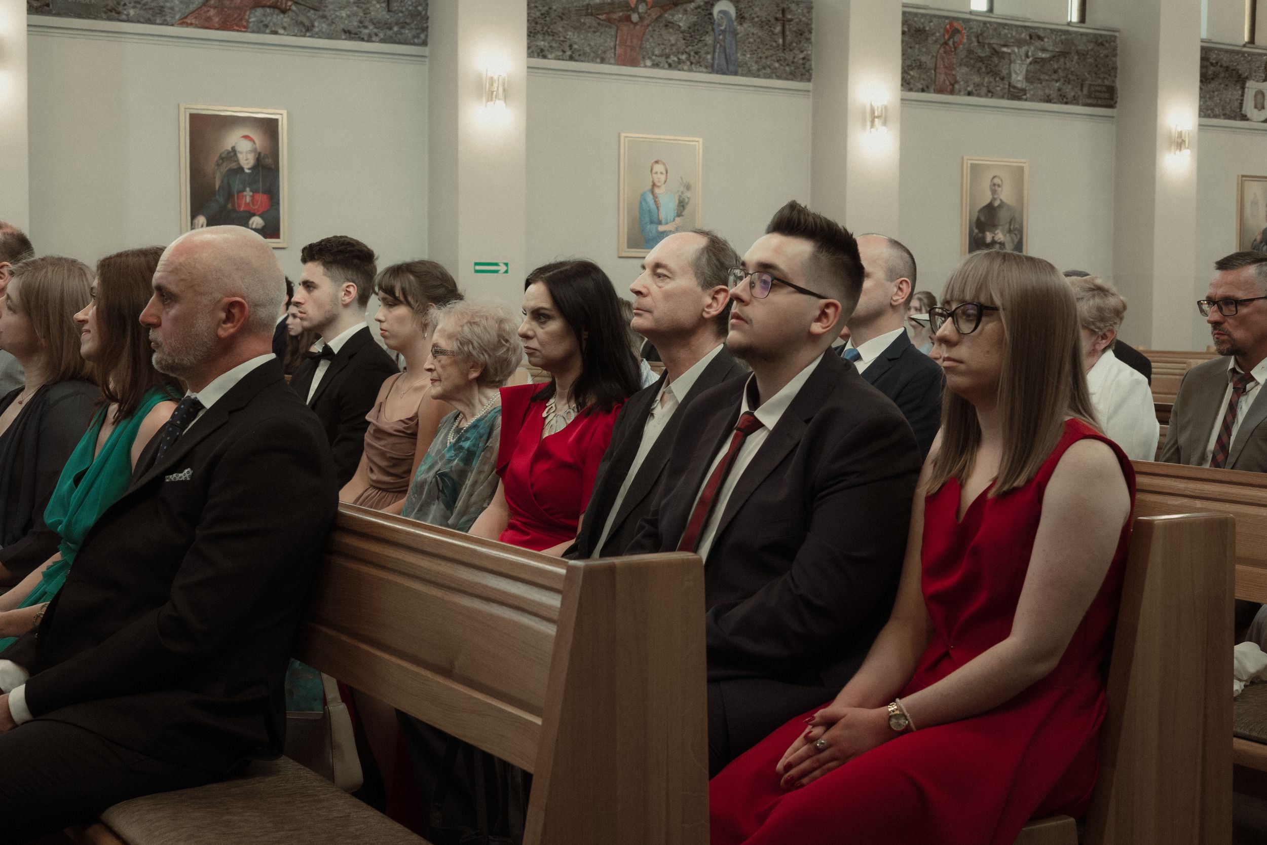Wedding guests sit attentively in wooden church pews during a ceremony.