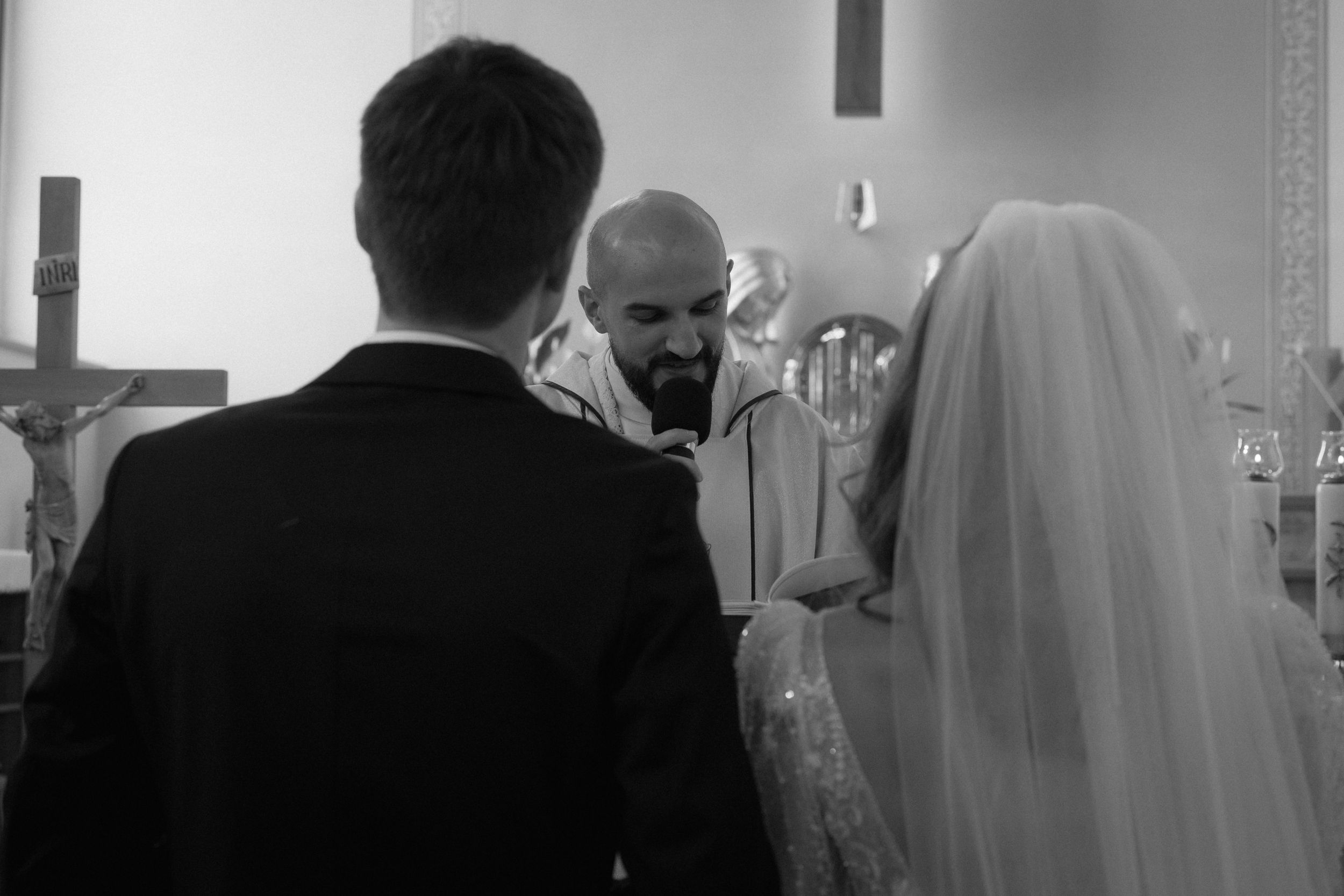 A black and white photograph of a wedding ceremony at a church altar with a priest officiating.