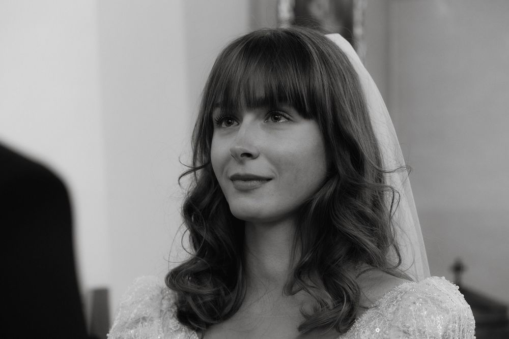 Bride in black and white photograph wearing wedding dress and veil with soft wavy hair and bangs.