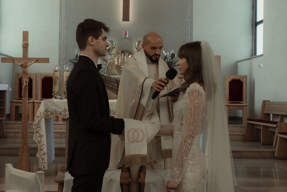 A couple exchanges vows during a church wedding ceremony as a priest officiates at the altar.