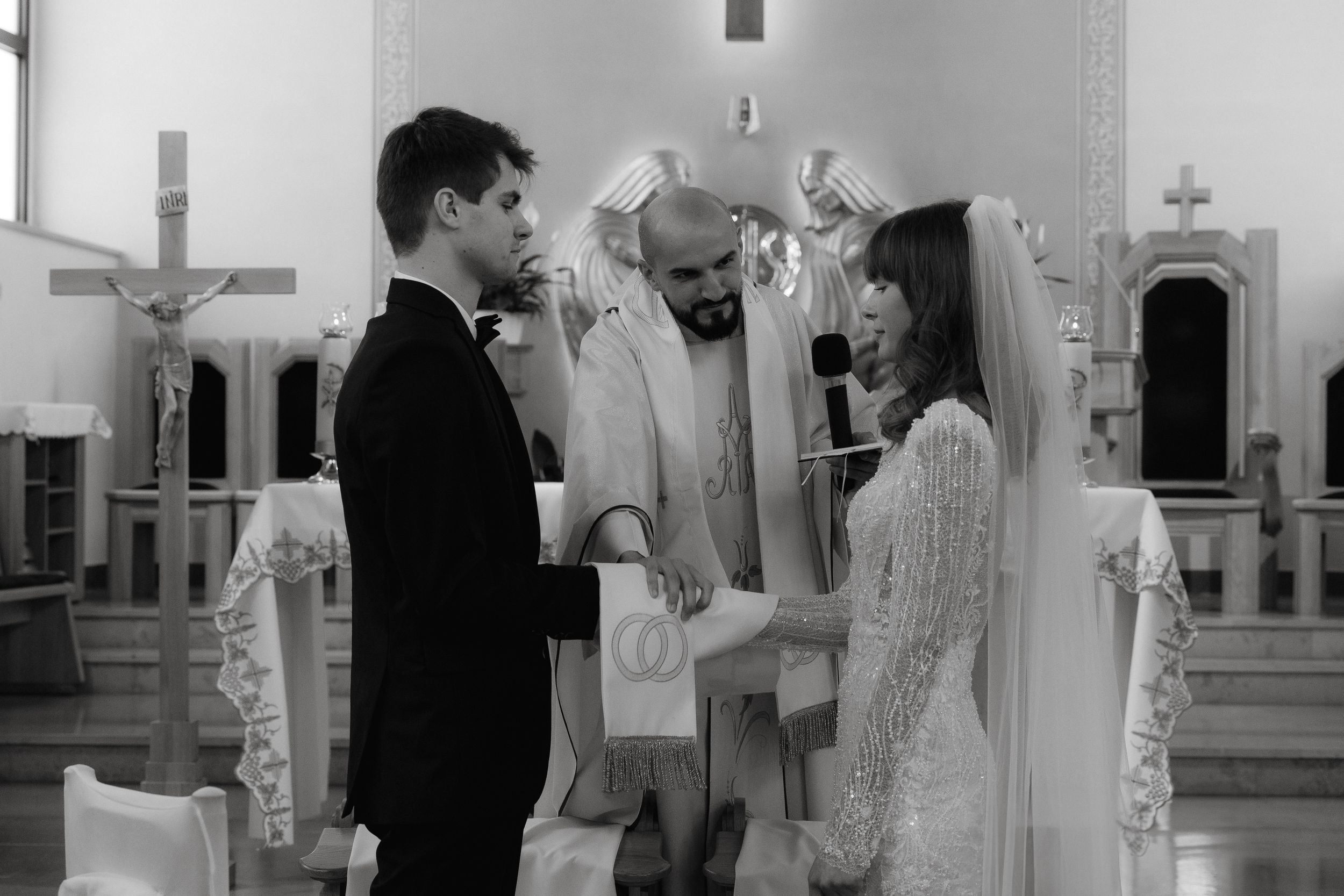 Black and white photograph of a traditional wedding ceremony taking place inside a church with religious crosses visible.