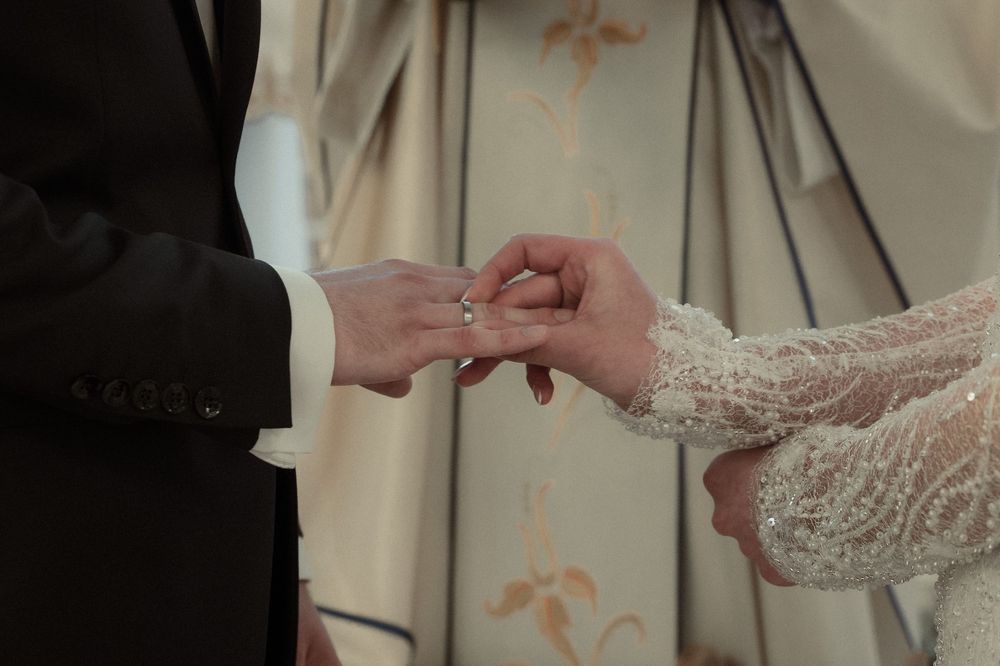 Close-up shot of hands exchanging wedding rings during a ceremony against a soft floral backdrop.