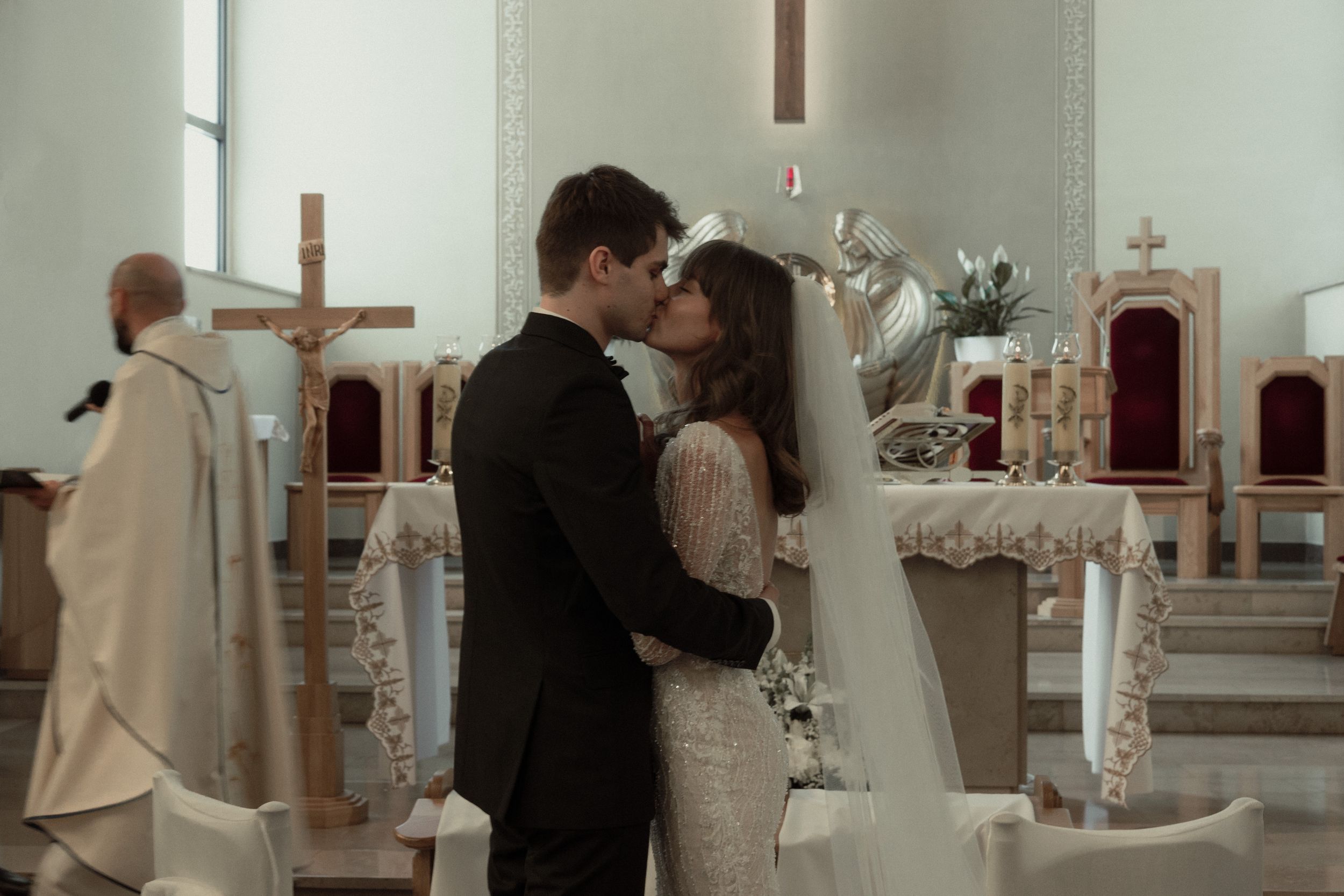 A romantic wedding ceremony in a white church interior with cross and altar decorations.