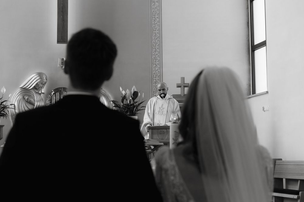 Black and white photo from behind a couple at a wedding ceremony with an officiant standing at the altar.