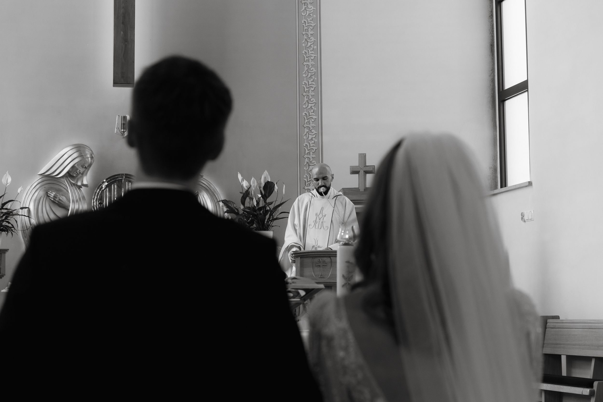 Black and white photo from behind a couple at a wedding ceremony with an officiant standing at the altar.