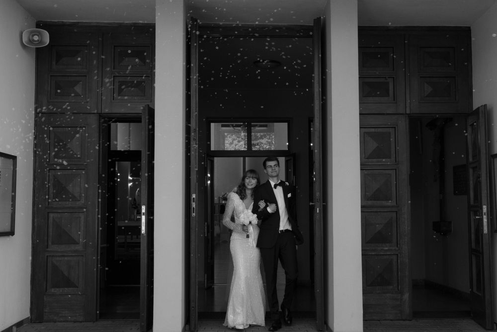 Black and white vintage-style photograph of figures standing in a doorway framed by tall decorative columns.