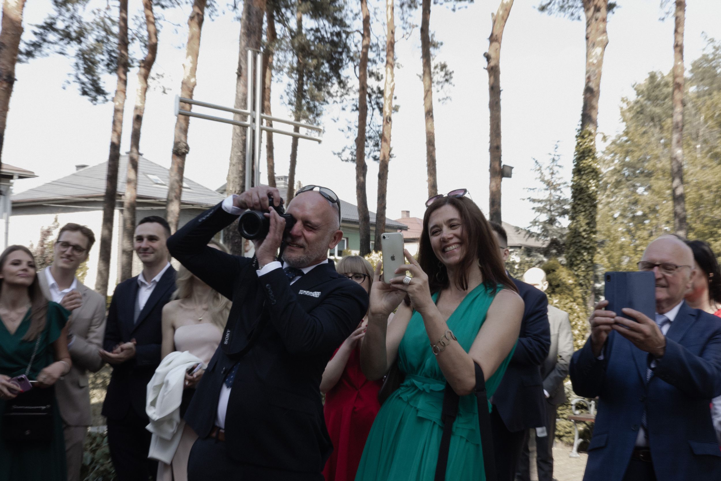 Wedding guests applaud and celebrate outdoors among tall pine trees during a special moment at the ceremony.