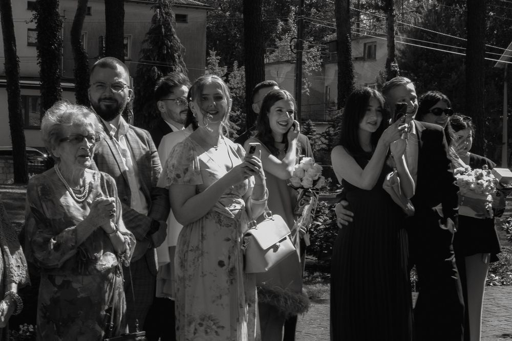 A series of spectators take photos at an event using their mobile phones in black and white.