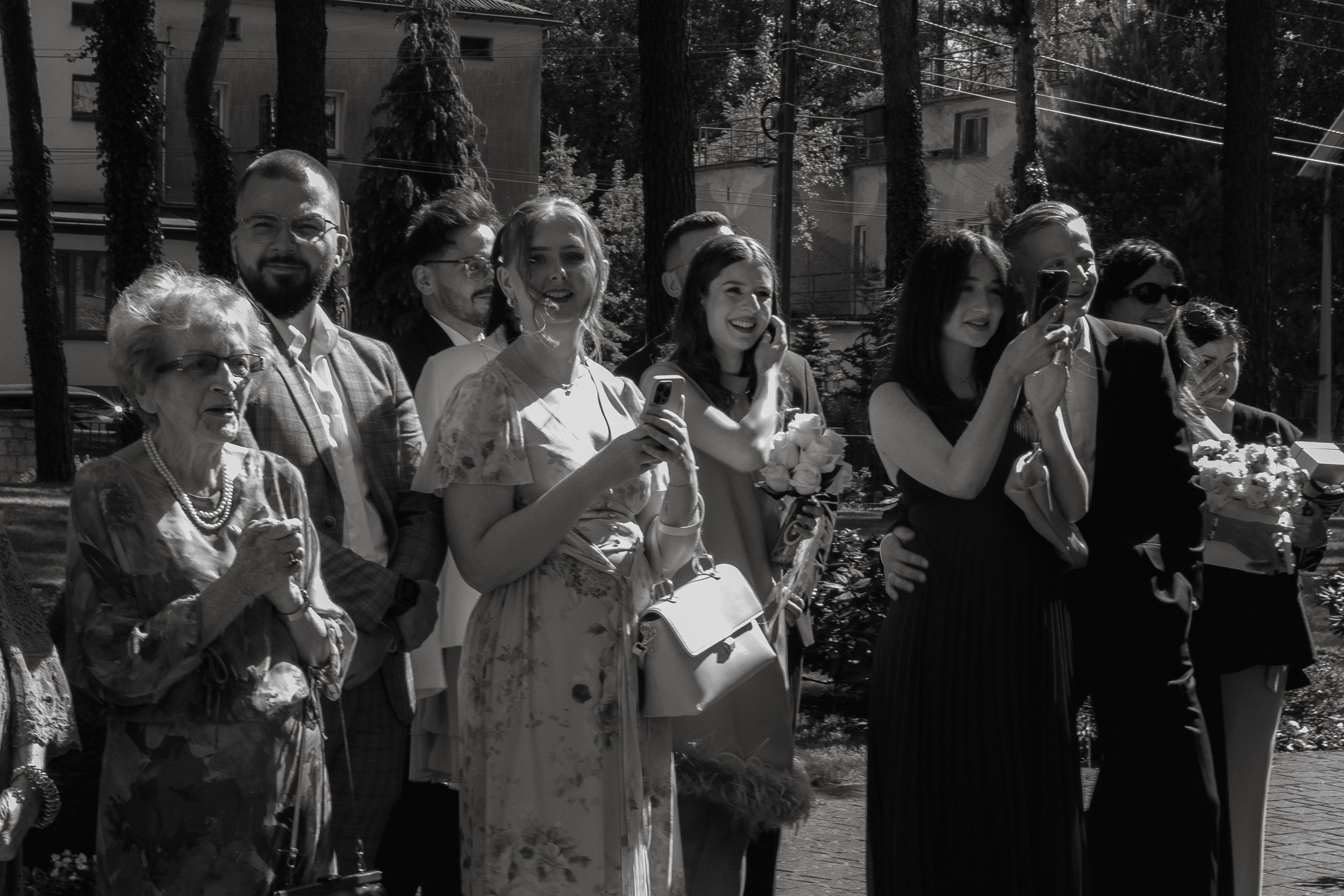 A series of spectators take photos at an event using their mobile phones in black and white.