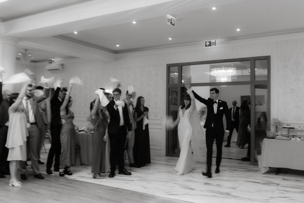 Black and white photo of a festive celebration with people dancing and mingling in a light-filled reception room.