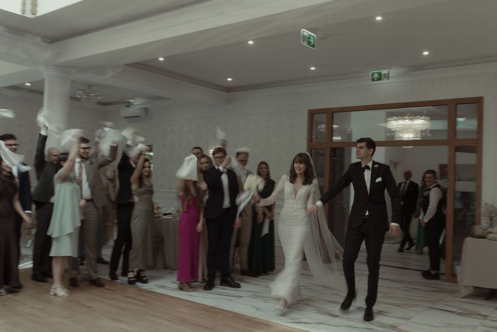 A couple and guests dance during their wedding celebration in a well-lit reception venue.