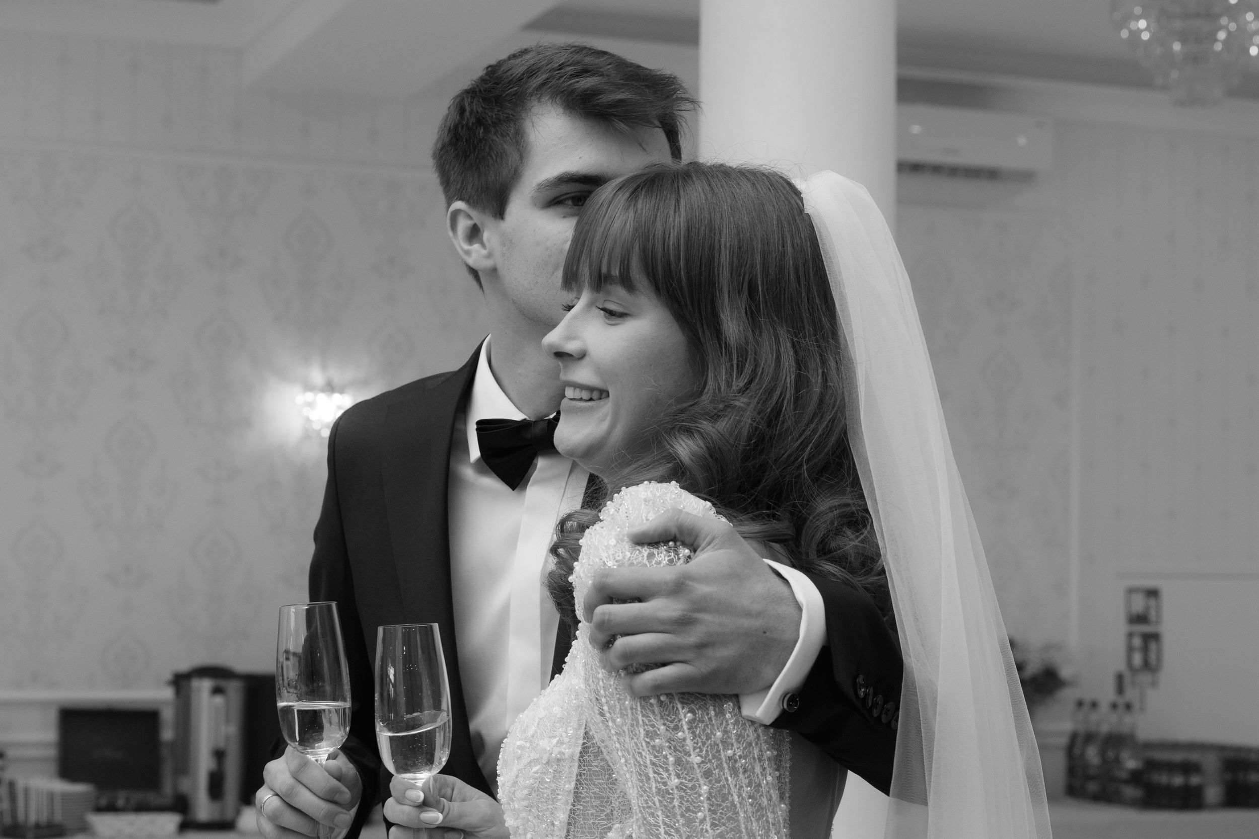 Two newlyweds share a tender embrace during their wedding reception in an elegant indoor setting.