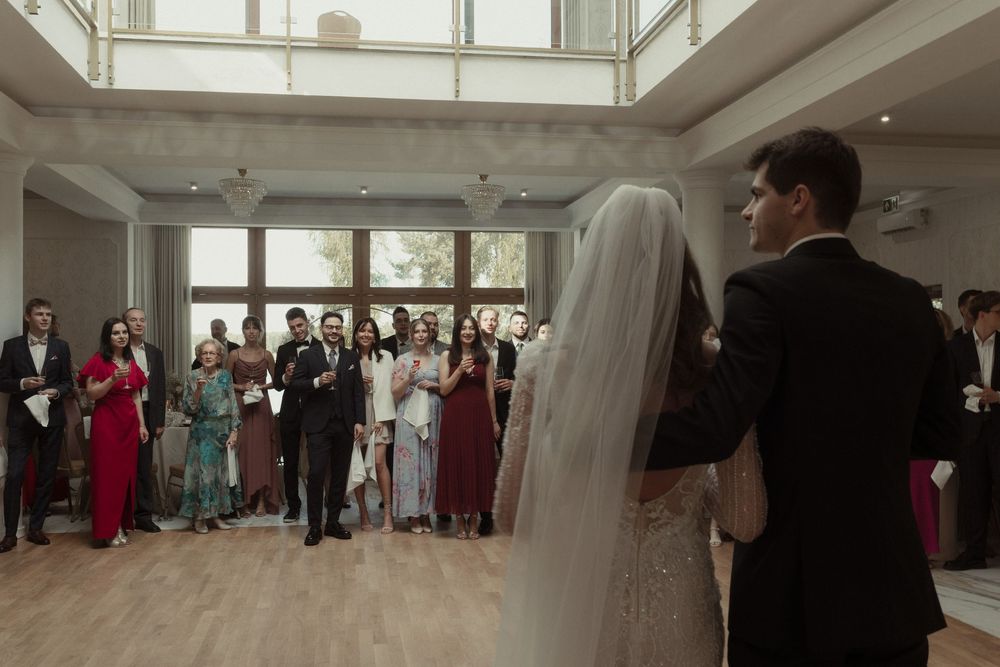 Wedding guests watch as newlyweds stand at the front of a bright indoor venue during their ceremony.