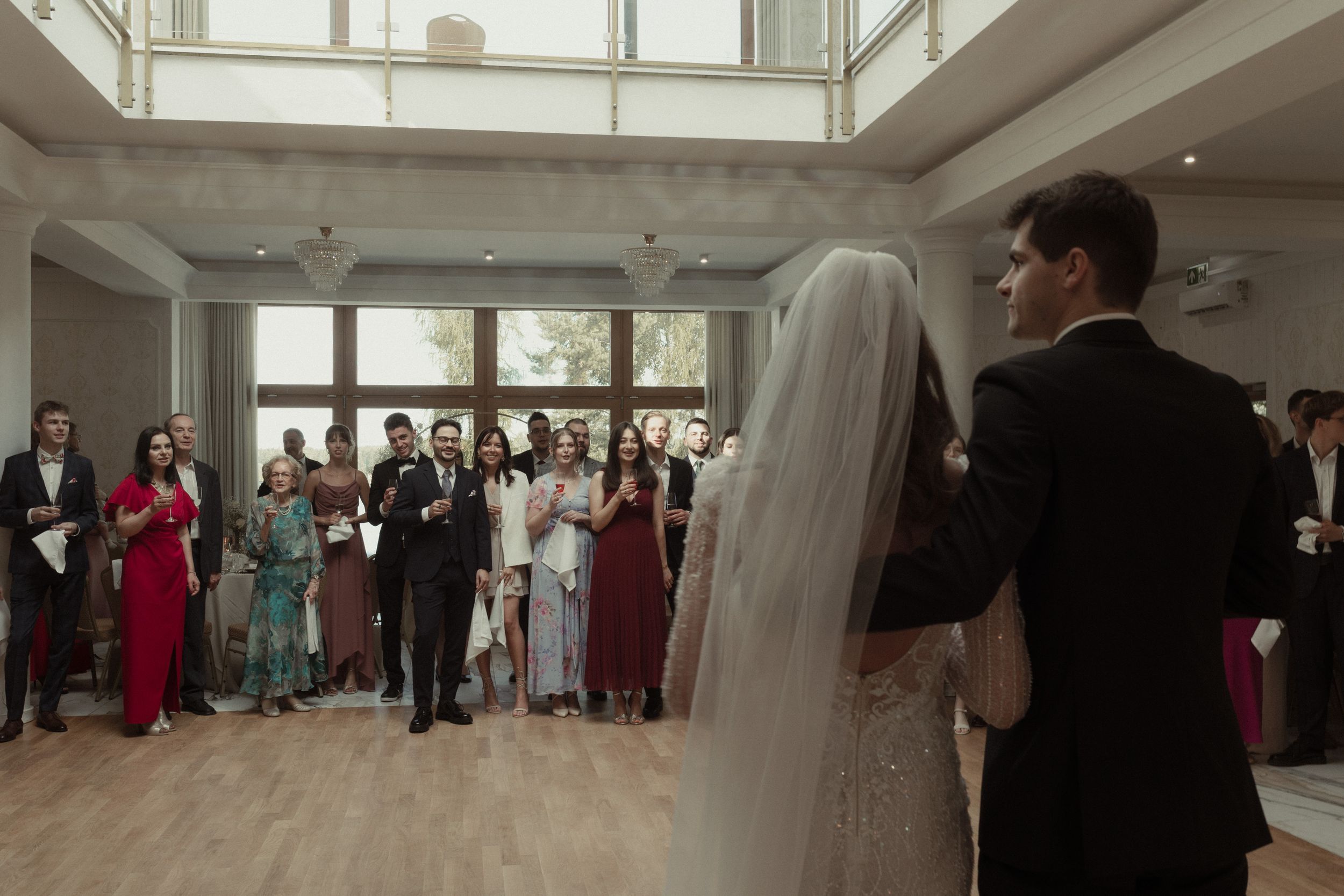 Wedding guests watch as newlyweds stand at the front of a bright indoor venue during their ceremony.