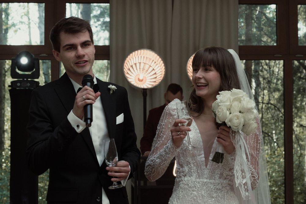 Newlyweds share a joyful moment at their wedding reception, holding microphones and drinks in a wood-paneled room.