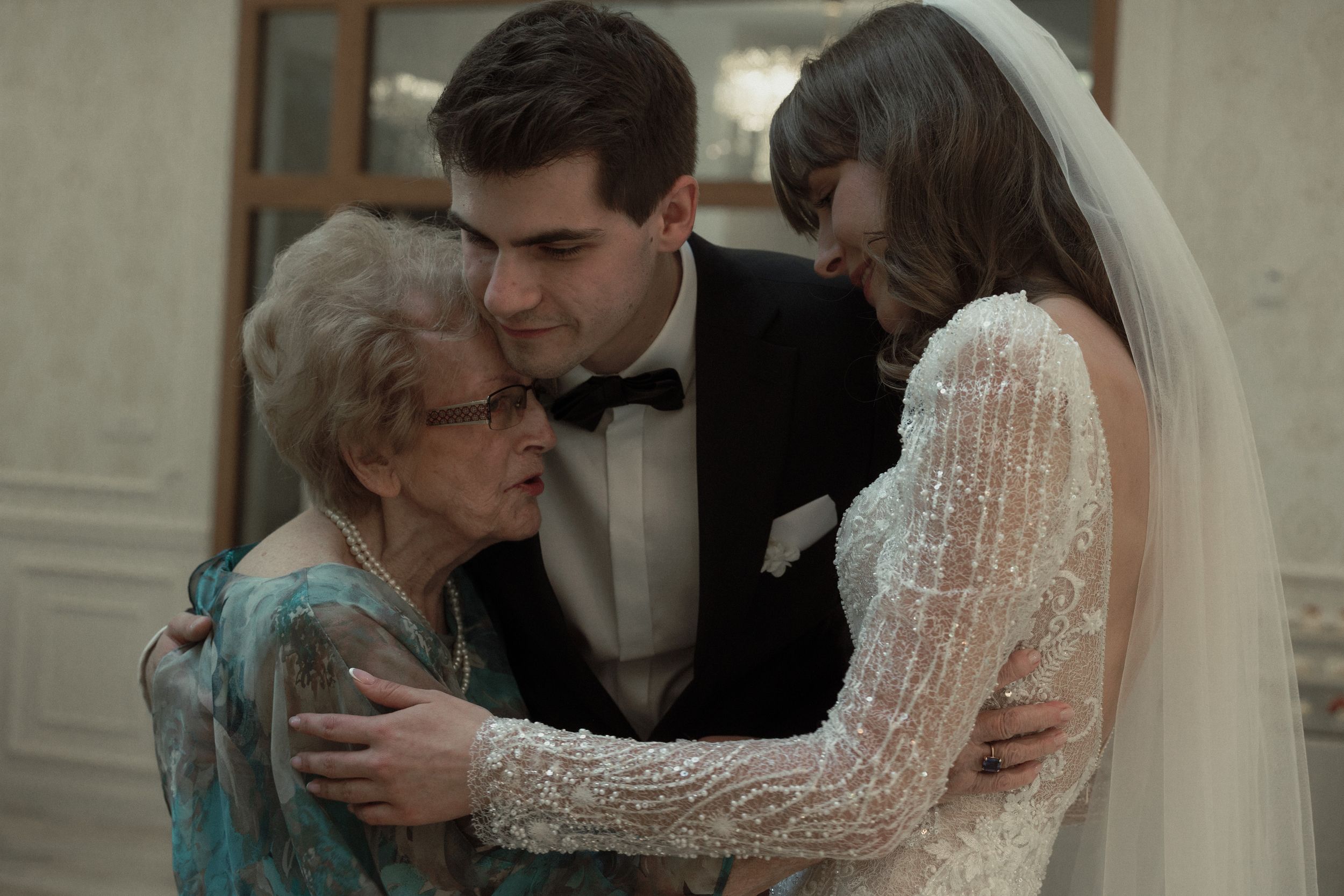 An emotional wedding moment shows a tender embrace between a bride in a lace sleeve gown and an elderly woman in blue.