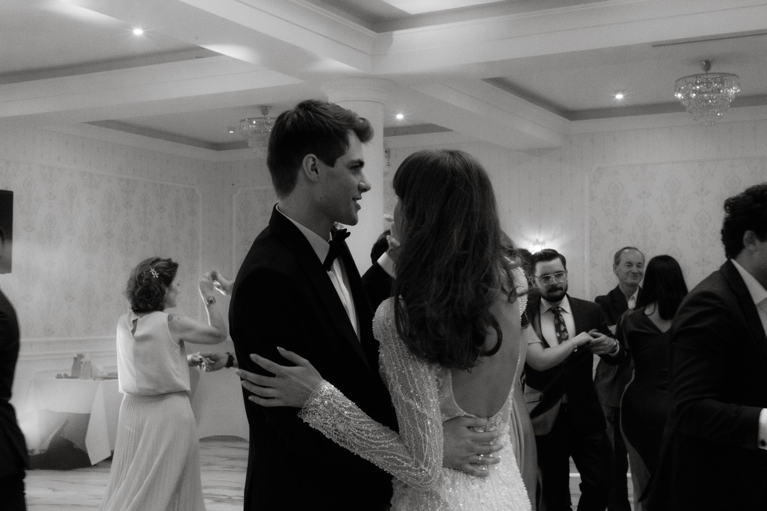 A couple shares an intimate dance moment at their wedding reception under elegant crystal chandeliers.