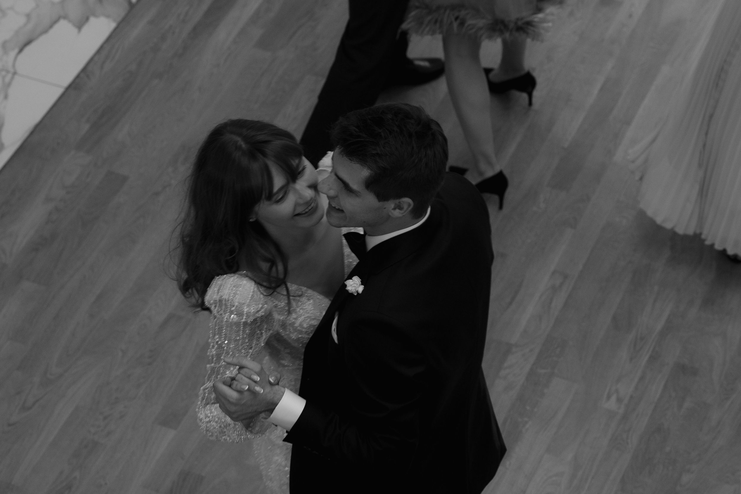A black and white photo captures a couple dancing intimately on a wooden dance floor during their wedding celebration.