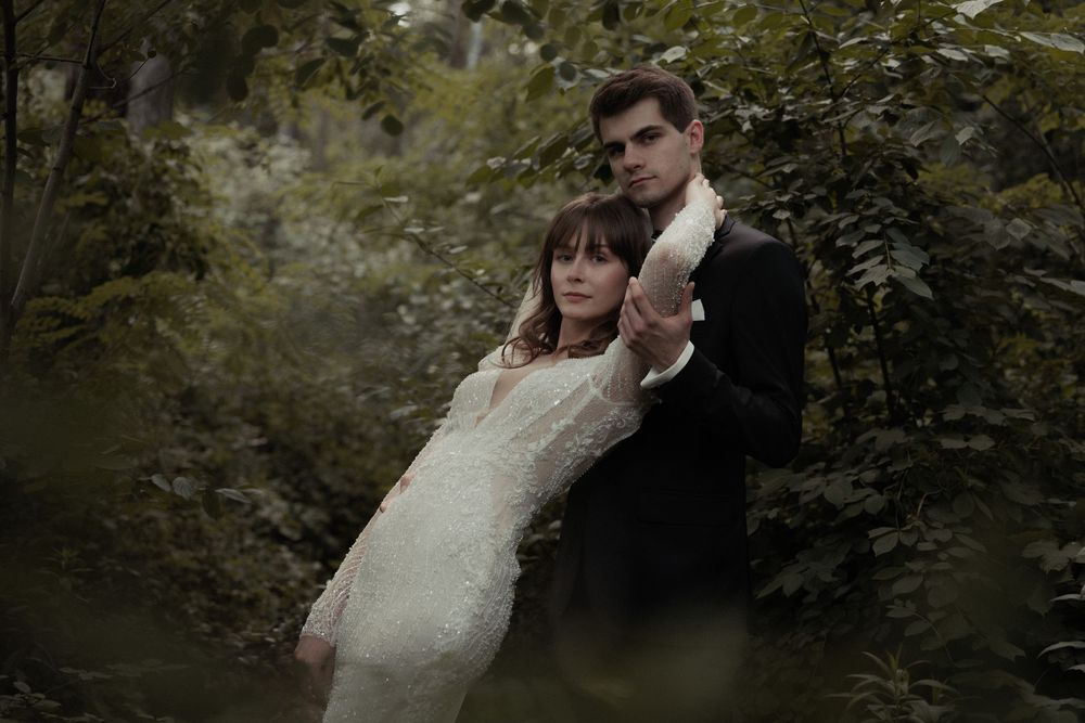 Wedding party walking under a lush green canopy of trees in a forest path during a romantic outdoor ceremony.