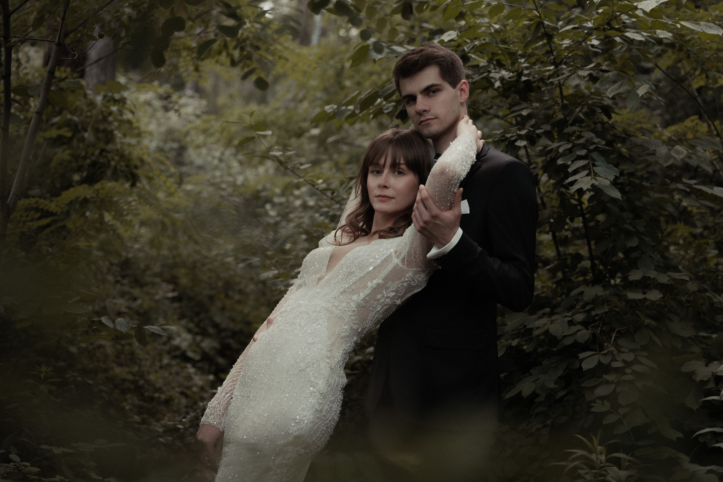 Wedding party walking under a lush green canopy of trees in a forest path during a romantic outdoor ceremony.