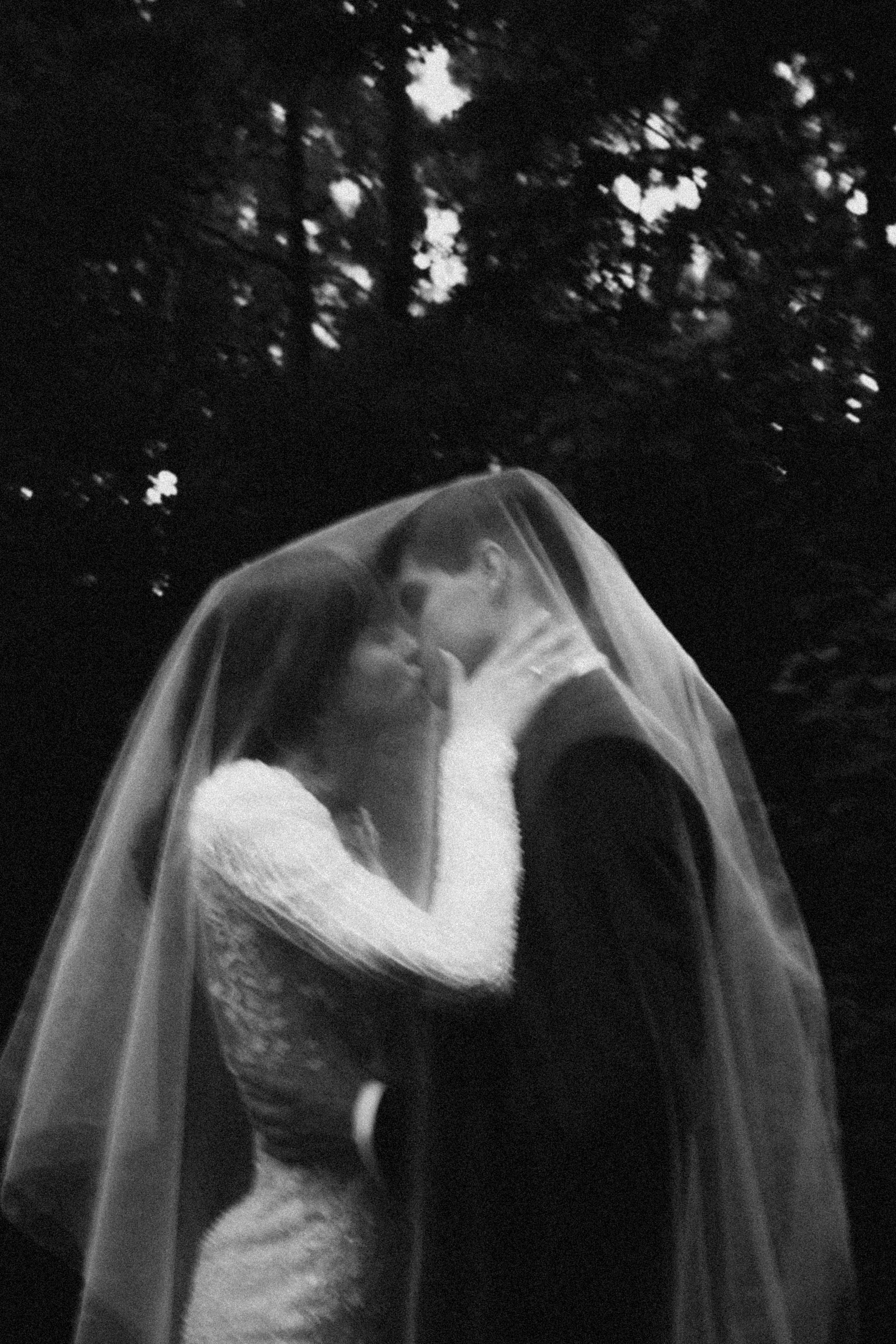 A romantic black and white wedding photo showing newlyweds sharing a tender kiss under a delicate veil.
